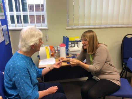 Elderly woman receiving hearing aid support from another woman