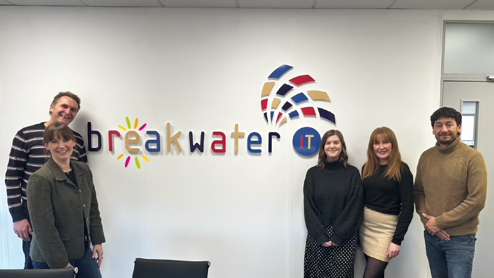Sarah and Peter from Break with Sam, Jordan and John from Breakwater IT in front of the Breakwater IT logo.