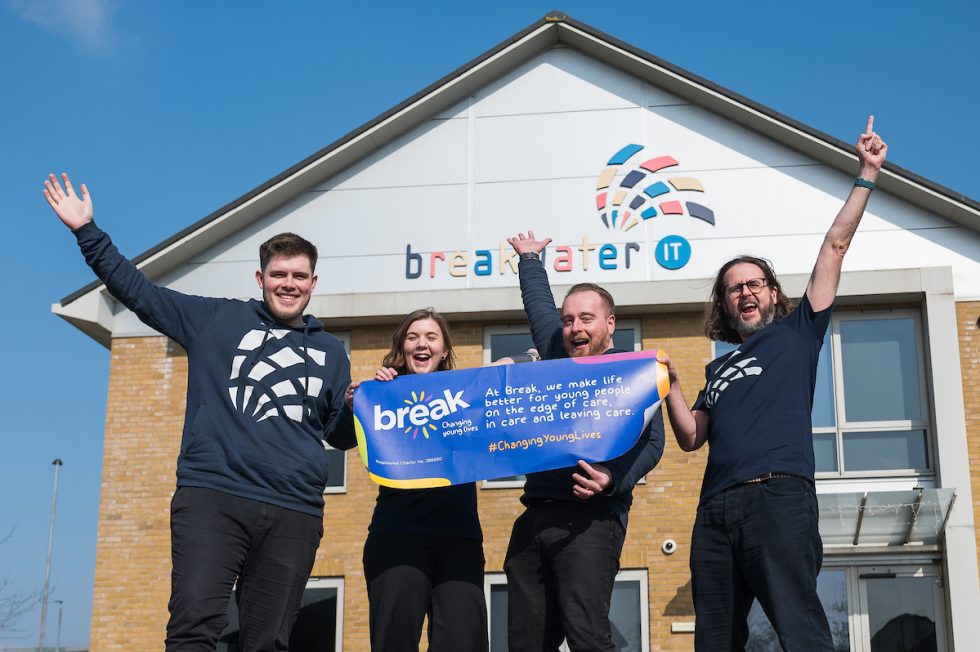 Toby, Sam, Dean and Andy outside the Breakwater IT office holding a Break banner.