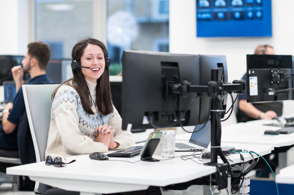 Jess wearing a headset sits at her desk, focused on two computer screens in front of her.