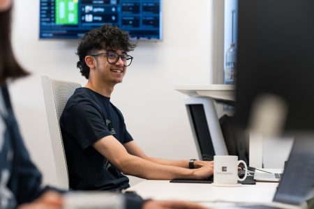 A man wearing glasses sits at a desk, focused on his computer screen.