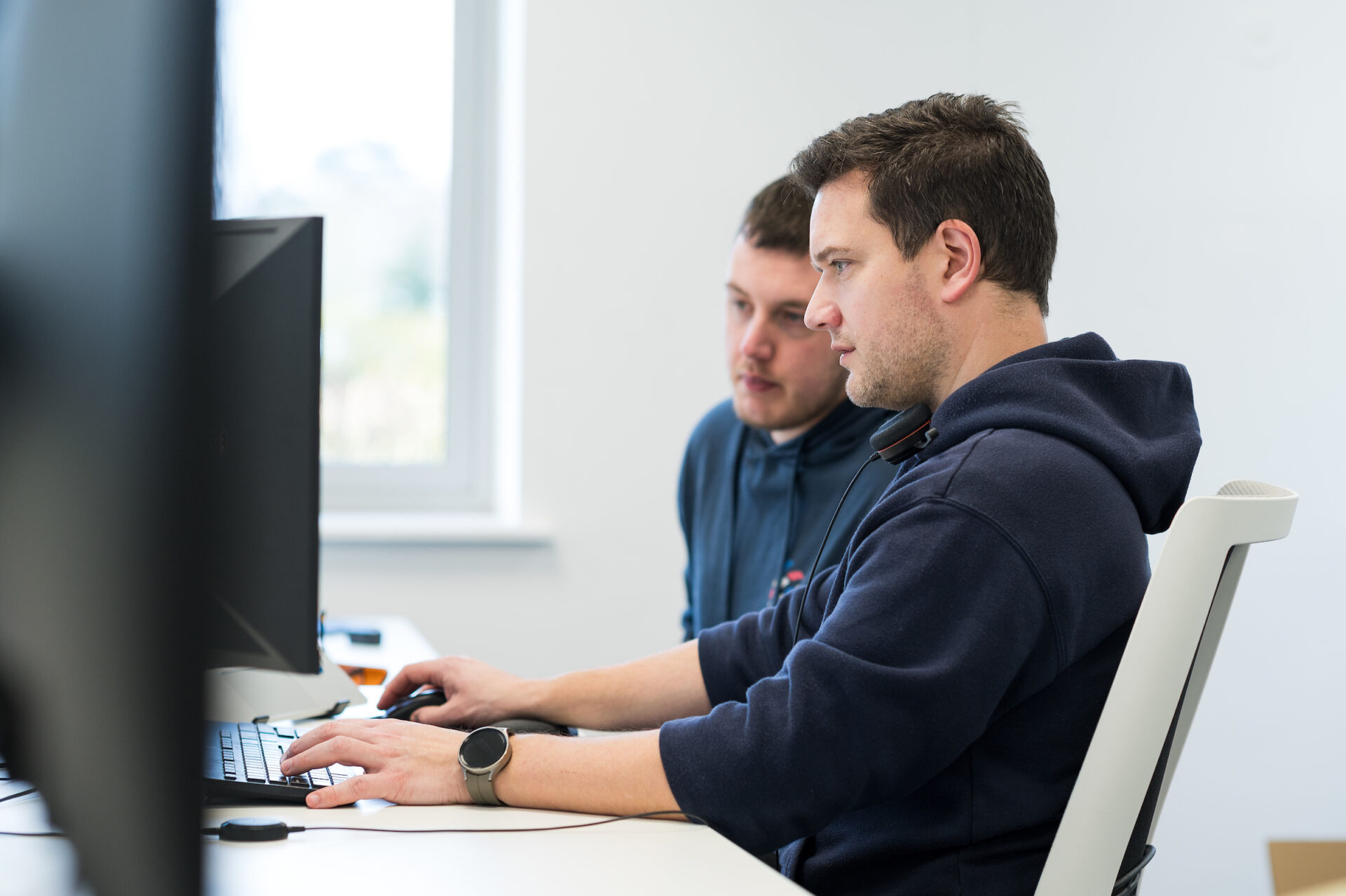 Bryce and John sitting at their desks focusing on one computer screen.