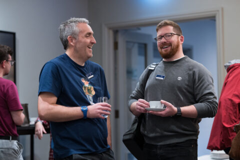 Two men stood smiling and chatting.