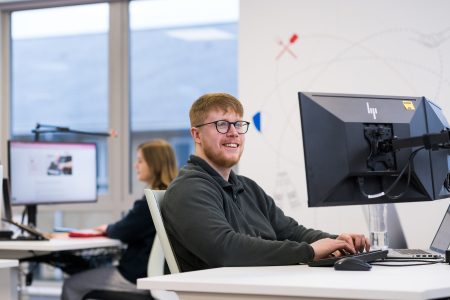 James smiling at his computer screen, sitting at his desk in an office.