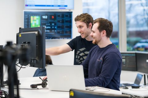 Two colleagues engaged in a discussion while working on a computer in a bright office environment.