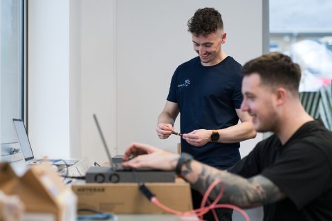 Two colleagues engaged in a discussion while working on a laptop in a bright office environment.