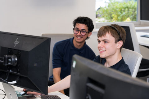 Jonathan and Aqeel smiling at Jonathan's monitor in the office