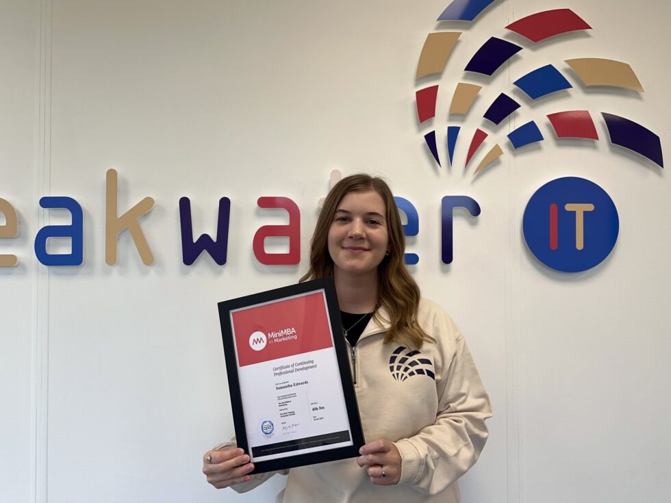 Sam holding Mini MBA in Marketing certificate in front of the Breakwater IT logo