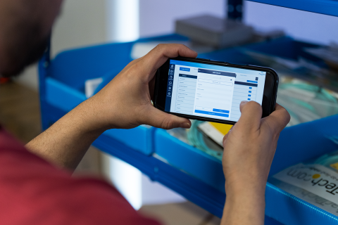A man holding a phone showing a stock management application