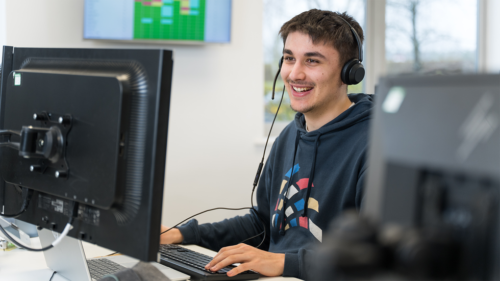 Oliver wearing a headset at his desk in the office.