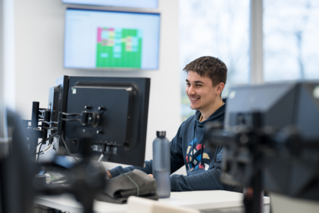 Oliver is sat at his desk looking at this monitor. There is a screen behind him displaying data.